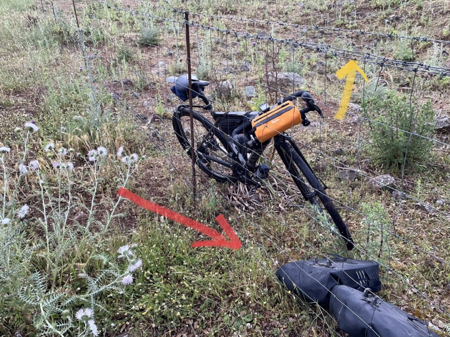 La mia bici appoggiata su un recinto con filo spinato. Due frecce indicano il filo e il fondo del recinto
